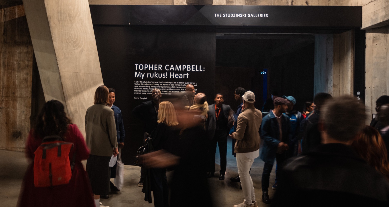 Visitors gathered beneath the Topher Campbell My rukus! Heart exhibition title