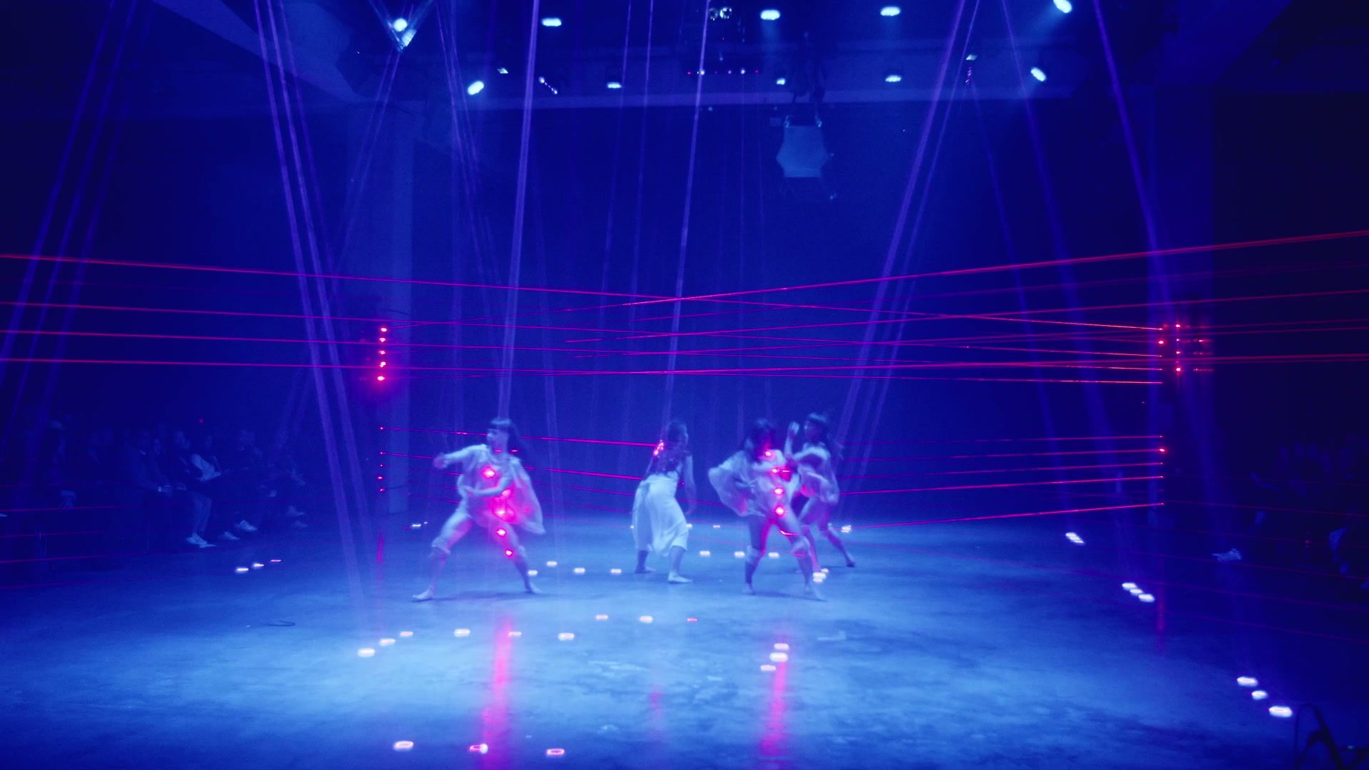 Ensemble of performers moving together inside a red laser grid