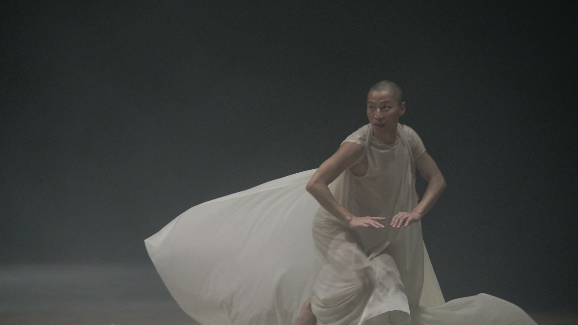 A performer moving with a long white train in a softly lit space